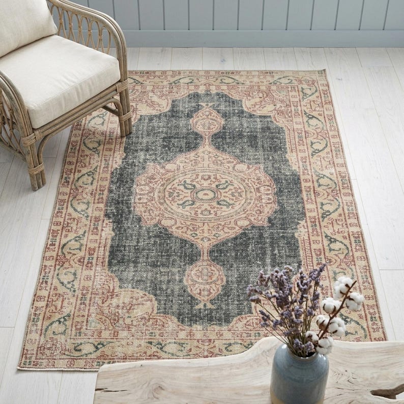 a rug with a floral design, a wicker chair, and a wooden coffee table with a vase of purple flowers.