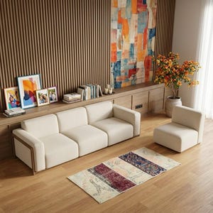 Könnte beinhalten: Ein modernes Wohnzimmer mit einem cremefarbenen Ecksofa und einem Sessel. Ein farbenfrohes abstraktes Gemälde hängt über einem Holzschrank. Ein gemusterter Teppich liegt auf dem Holzboden, mit gerahmten Kunstwerken und Büchern.