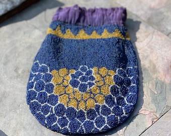 May include: A blue beaded bag with a gold and white geometric design. The bag has a purple fabric lining.