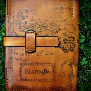 May include: A brown leather journal with a map of Narnia printed on the cover. The journal has a leather strap closure and is decorated with a Celtic knot border.