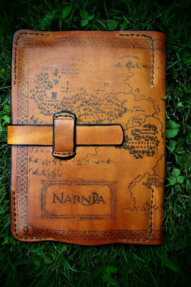 May include: A brown leather journal with a map of Narnia printed on the cover. The journal has a leather strap closure and is decorated with a Celtic knot border.