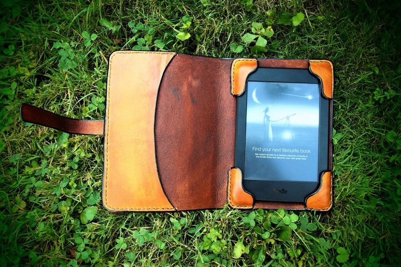 May include: A brown leather case with a flap closure for an e-reader. The e-reader is open and shows a screen with the text "Find your next favourite book".