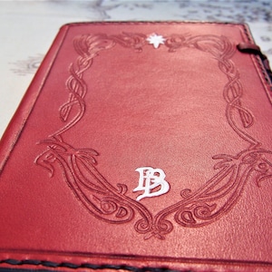 Puede incluir: Diario de cuero rojo con un dise&ntilde;o decorativo en relieve que presenta una estrella y un monograma "B".