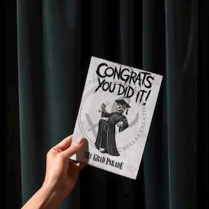 May include: A graduation card with the text "CONGRATS YOU DID IT!" and "THE GRAD PARADE". The card features a skeleton in a graduation gown holding a diploma. The card is held against a dark green curtain.