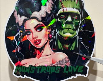 May include: A sticker featuring a stylized illustration of the Bride of Frankenstein and Frankenstein's monster. The Bride has black hair with white accents, blue eyes, and red lips. The monster is green. The text "MONSTROUS LOVE" is at the bottom.