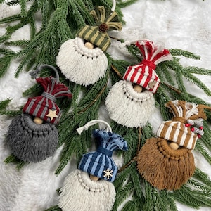 May include: A collection of handmade gnome ornaments with various colored hats and beards. The hats are striped or solid, in colors like red, blue, and green. The beards are made of white, gray, and brown macrame. Each ornament has a wooden bead face.