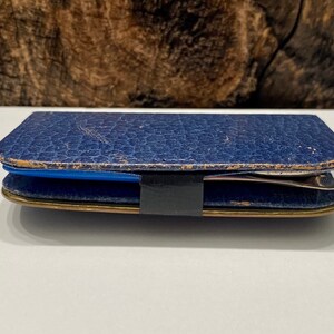 May include: A blue leather case with a gold trim and a black strap. The case is closed and appears to be empty.