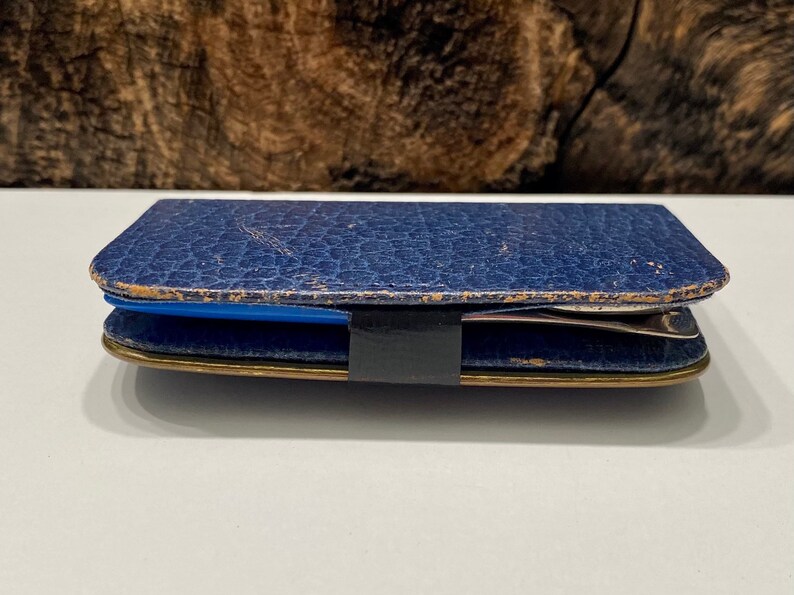 May include: A blue leather case with a gold trim and a black strap. The case is closed and appears to be empty.
