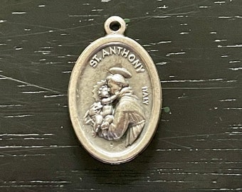 May include: Oval-shaped silver pendant featuring a detailed relief of St. Anthony holding a child. The text "ST. ANTHONY ITALY" is inscribed around the top edge. The pendant has a small loop at the top for attachment.