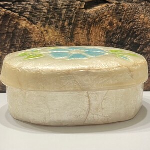 May include: A white oval trinket box with a blue and green floral design on the lid.