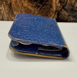 May include: A blue leather wallet with a worn, textured surface. The wallet is closed and has a brass clasp.