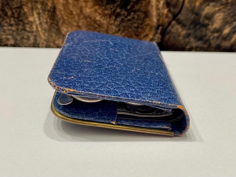 May include: A blue leather wallet with a worn, textured surface. The wallet is closed and has a brass clasp.