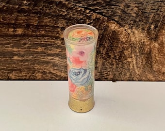 May include: A floral patterned lipstick tube with a gold base and a clear plastic top.