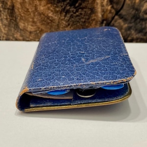 May include: A blue leather wallet with a worn, textured surface. The wallet is closed and has a gold metal trim.