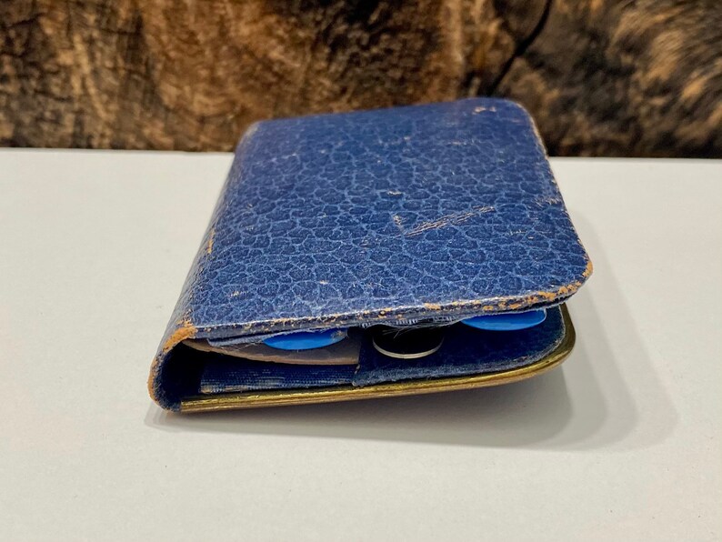 May include: A blue leather wallet with a worn, textured surface. The wallet is closed and has a gold metal trim.
