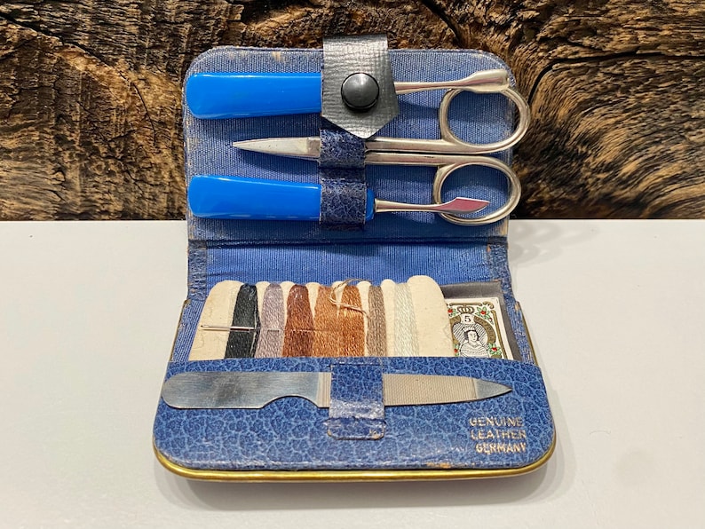 May include: A blue leather travel sewing kit with a variety of tools, including scissors, a needle threader, and a nail file. The kit also includes spools of thread and a small card with the text "Genuine Leather Germany".