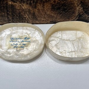 May include: An oval-shaped, white, paper mache box with a blue inscription that reads "Salvador - Leah Mendon, Vermont July 6, 1991". The box is open and the inside is lined with white paper.