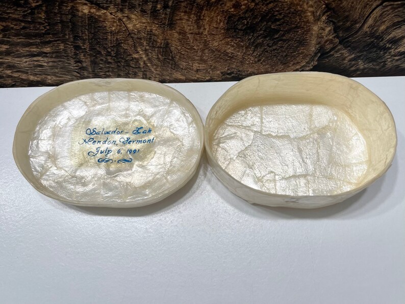 May include: An oval-shaped, white, paper mache box with a blue inscription that reads "Salvador - Leah Mendon, Vermont July 6, 1991". The box is open and the inside is lined with white paper.