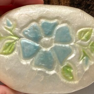 May include: A white oval-shaped trinket box with a raised design of a blue flower with green leaves.