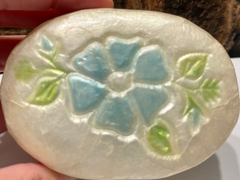 May include: A white oval-shaped trinket box with a raised design of a blue flower with green leaves.