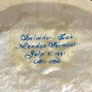 May include: Close-up of a white, textured surface with blue ink inscription: "Salvador - Zak Mendon, Vermont July 6, 1991".