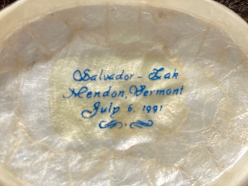 May include: Close-up of a white, textured surface with blue ink inscription: "Salvador - Zak Mendon, Vermont July 6, 1991".