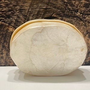 May include: A white, oval-shaped box made of mother of pearl. The box has a smooth, glossy finish and a slightly raised lid.