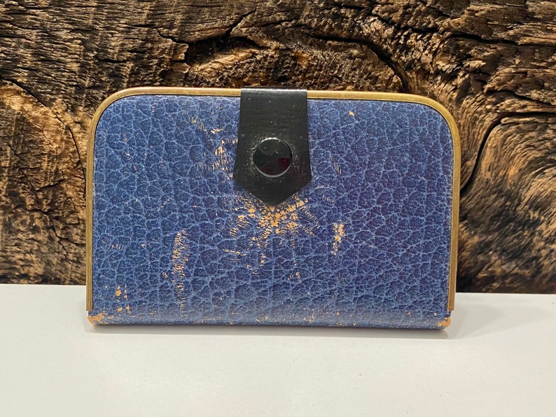 May include: A blue leather card holder with a gold trim and a black button closure.