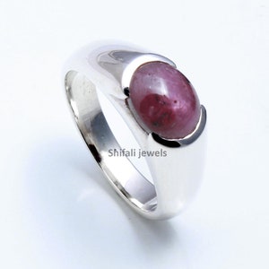 Peut inclure: Une bague en argent avec une pierre ovale rouge. La bague a une bande lisse et arrondie.