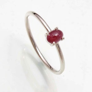 May include: A silver ring featuring a vibrant, oval-shaped ruby gemstone. The ring's band is slender and polished, with the ruby securely set in a four-prong setting. The ruby has a deep red color, adding a touch of elegance.