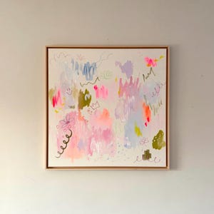Könnte beinhalten: Abstrakte Kunstmalerei in einem Holzrahmen. Das Kunstwerk zeigt eine Mischung aus rosa, blauen, grünen und gelben Pinselstrichen und Kritzeleien auf cremefarbenem Hintergrund. Das Gemälde wirkt skurril und verspielt.