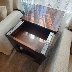 May include: A dark wood end table with a sliding top that reveals a storage compartment. The table is sitting on a beige carpet.