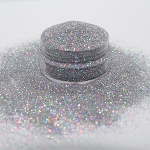 May include: A clear jar filled with iridescent silver glitter, with a small amount of glitter spilled out around the jar.