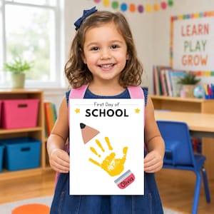 Young student holding a completed First Day of School handprint printable in a classroom.