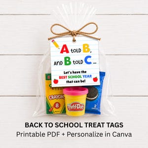 May include: A clear plastic treat bag tied with brown twine, containing a yellow box of crayons, a small yellow container of modeling compound, and a blue package of cookies. A white tag features the text A told B, and B told C... Let's have the BEST SCHOOL YEAR that can be! with a pencil and apple graphics.