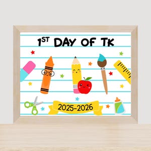 May include: A framed print with a school theme. The print features the text "1st Day of TK" above cartoon illustrations of school supplies, including a pencil, crayon, apple, and scissors. The banner reads "2025-2026".