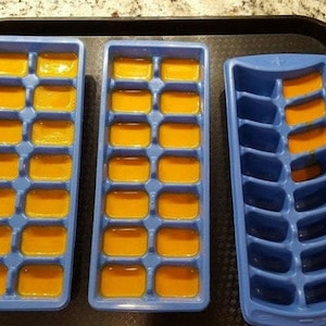 May include: Three blue ice cube trays, two filled with orange liquid and one empty. The trays are on a black tray.