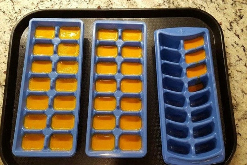 May include: Three blue ice cube trays, two filled with orange liquid and one empty. The trays are on a black tray.