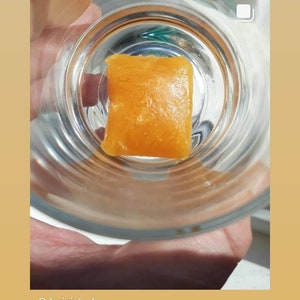 May include: A close-up of a small, square, orange-colored gummy candy in a clear glass dish. The candy has a slightly textured surface. The text "@REVIVAL7.IMMUNITY" is visible below the image.
