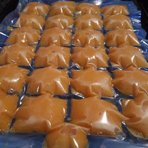 May include: A tray of 24 individual pouches filled with a light orange liquid, likely a fruit juice or smoothie, ready to be frozen into ice pops.