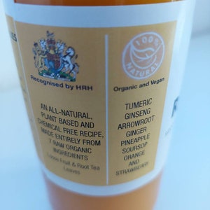 May include: A yellow bottle of juice with a white label. The label says "Recognised by HRH" and "Organic and Vegan". The ingredients listed are: Tumeric, Ginseng, Arrowroot, Ginger, Pineapple, Soursop, Orange, and Strawberry.