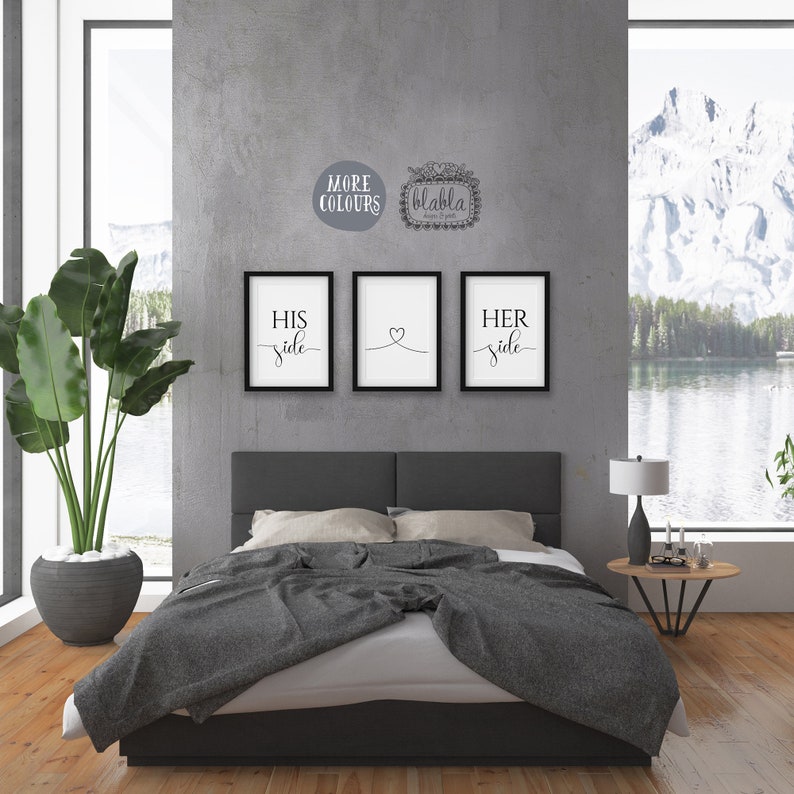 May include: Three black framed prints with white text on a grey wall. The prints read "His side", "Her side", and a heart symbol. The prints are hanging above a grey bed with a grey blanket and white pillows.