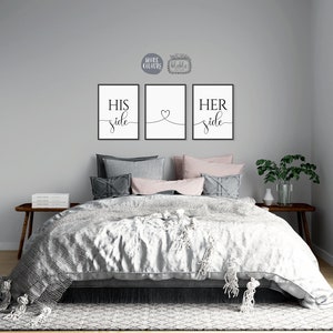 May include: Three black and white prints with the words "His side", "Her side" and a heart symbol. The prints are hanging on a grey wall above a bed with grey and pink bedding.