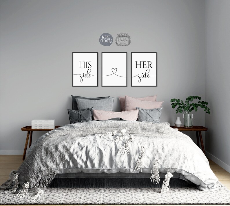 May include: Three black and white prints with the words "His side", "Her side" and a heart symbol. The prints are hanging on a grey wall above a bed with grey and pink bedding.