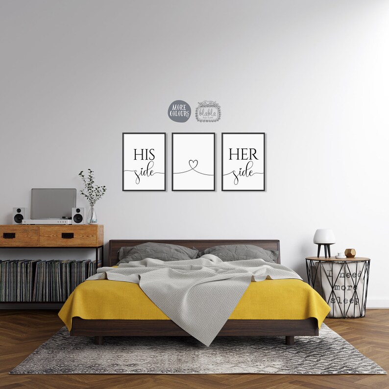 May include: Three black framed prints with white text on a white wall. The prints read "His side", a heart, and "Her side". The prints are hanging above a bed with a yellow blanket and a grey throw.