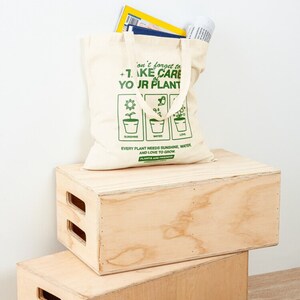 May include: A beige canvas tote bag with green text that reads "Don't forget to take care of your plants. Every plant needs sunshine, water, and love to grow. Plants are friends."
