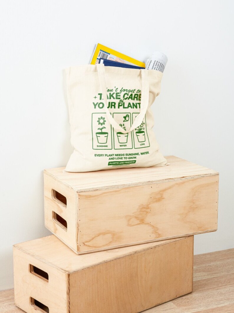 May include: A beige canvas tote bag with green text that reads "Don't forget to take care of your plants. Every plant needs sunshine, water, and love to grow. Plants are friends."
