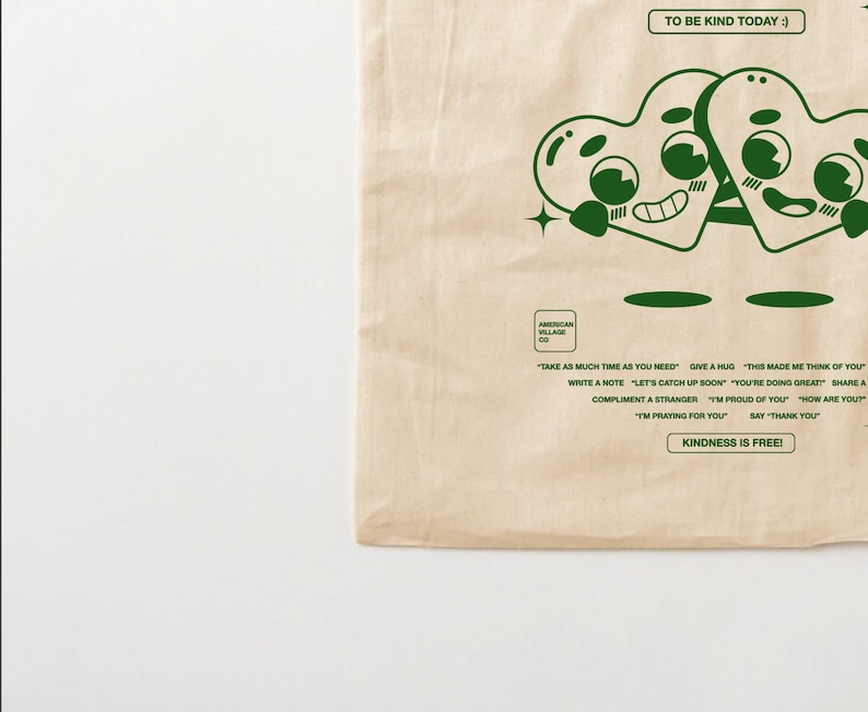May include: A beige tote bag with a green design of two cartoon hearts holding hands. The text "TO BE KIND TODAY :)" is at the top of the bag. The text "KINDNESS IS FREE!" is at the bottom of the bag. The text "AMERICAN VILLAGE CO" is in the center of the bag.