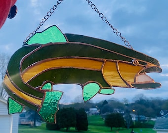May include: A stained glass fish with green, yellow, and brown glass pieces. The fish is hanging from a copper chain.