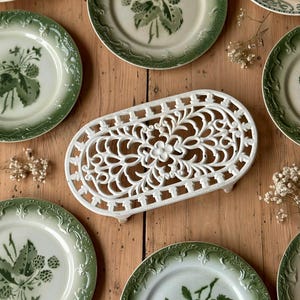 Peut inclure: Plusieurs assiettes anciennes avec des motifs verts et blancs, représentant des illustrations botaniques de fraises et de poires. Un dessous-de-plat blanc et orné est au centre. L'ensemble est disposé sur une surface en bois, pour un style vintage.